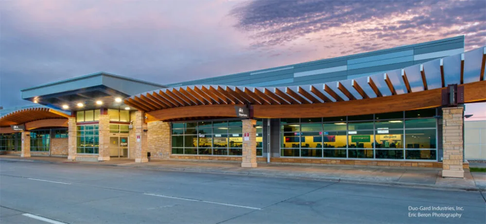 Curved glulam and translucent entrance canopy running the length of a building facade at dusk